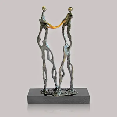 Zwei stilisierte Figuren in Bronze mit goldenem Verbindungsbogen auf einem dunklen Sockel.